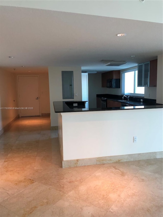 kitchen with dark countertops, a peninsula, black microwave, and a sink