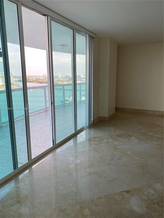 unfurnished room with baseboards, a water view, and expansive windows