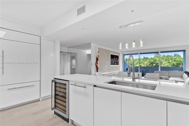 kitchen featuring a sink, white cabinetry, beverage cooler, and light countertops