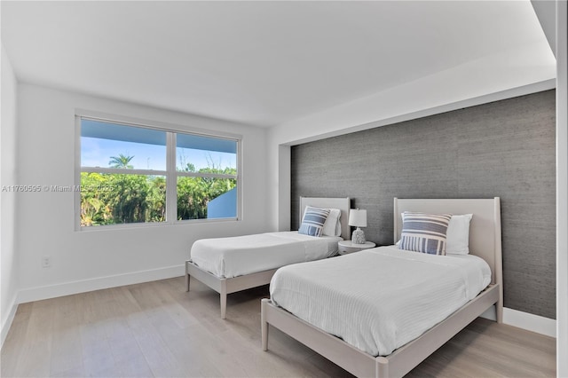 bedroom featuring an accent wall, light wood-style flooring, and baseboards