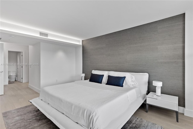 bedroom with an accent wall, wood finished floors, visible vents, and baseboards