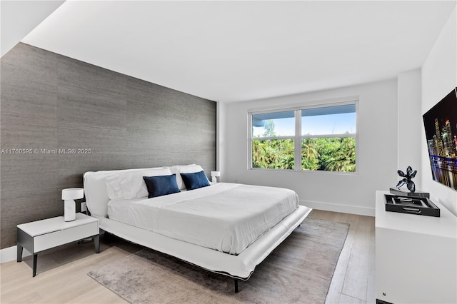 bedroom featuring baseboards, wood finished floors, an accent wall, and wallpapered walls