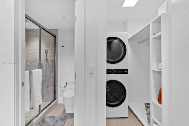 full bath featuring a stall shower, stacked washer / drying machine, toilet, and wood finished floors