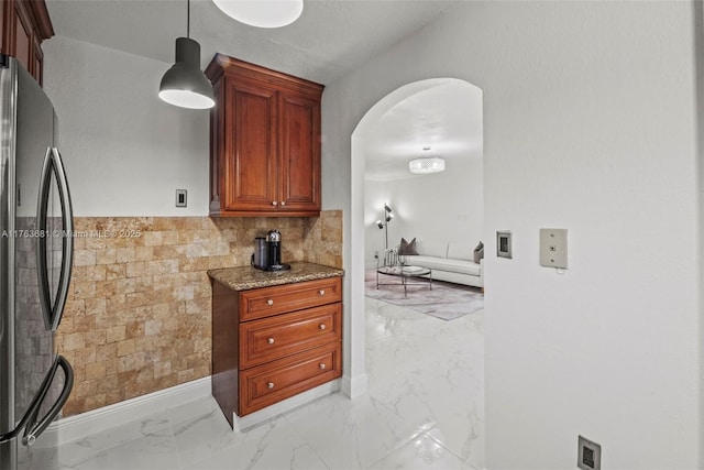 kitchen with stone countertops, arched walkways, freestanding refrigerator, pendant lighting, and marble finish floor