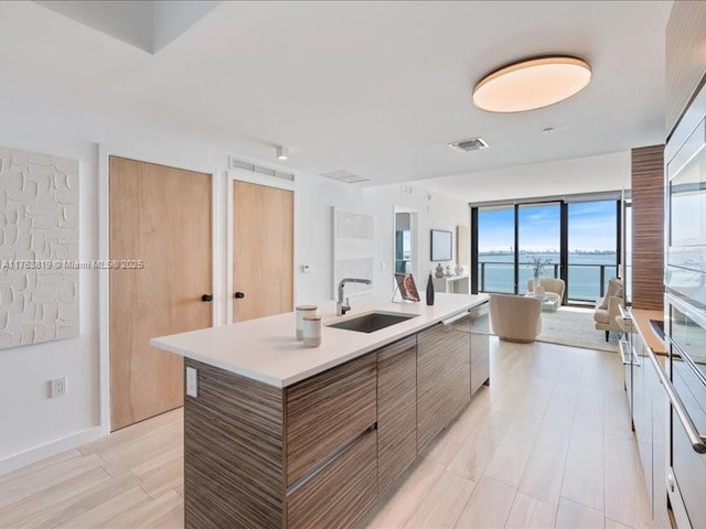 kitchen featuring visible vents, an island with sink, a sink, open floor plan, and light countertops