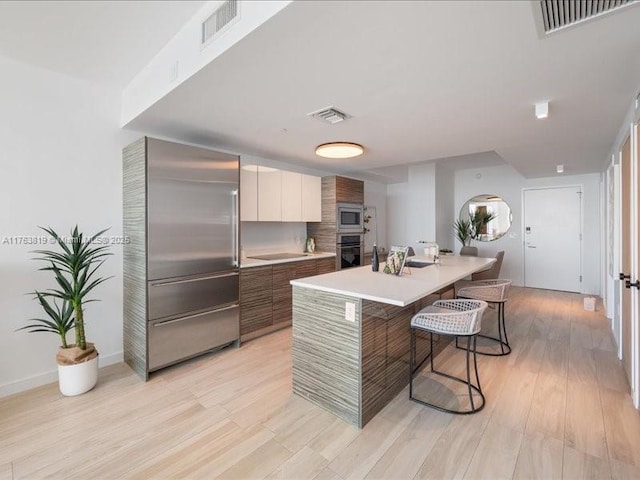 kitchen with visible vents, built in appliances, modern cabinets, and a kitchen bar