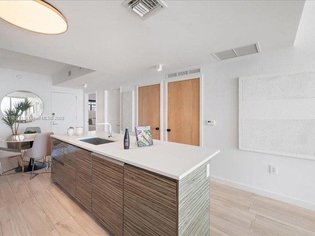 kitchen featuring a sink, visible vents, brown cabinets, and light countertops