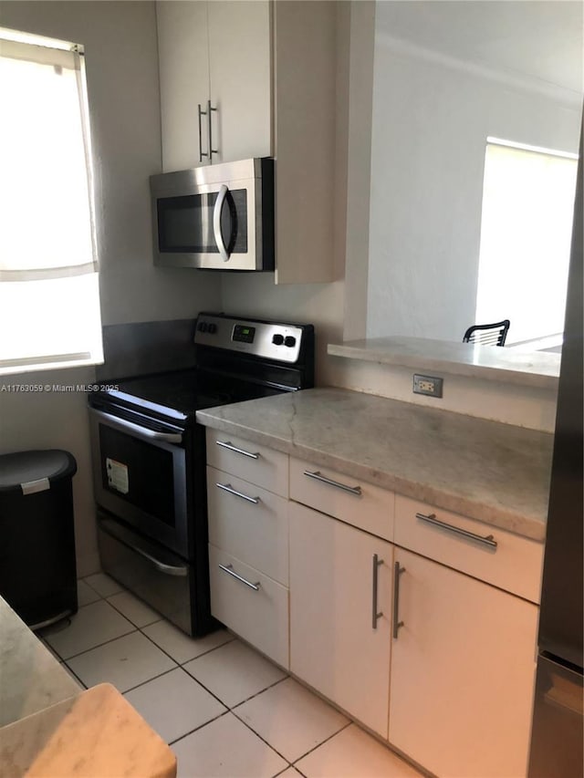 kitchen featuring white cabinets, light tile patterned floors, light stone countertops, and appliances with stainless steel finishes