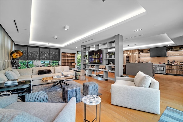 living area with a raised ceiling, bar, built in features, and wood finished floors