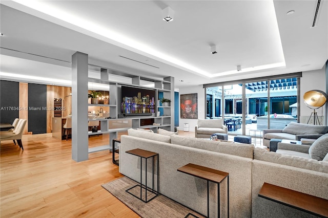 living area with a raised ceiling, built in features, light wood-style floors, and expansive windows