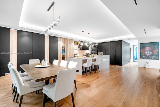 dining room featuring light wood-style flooring, rail lighting, and a raised ceiling