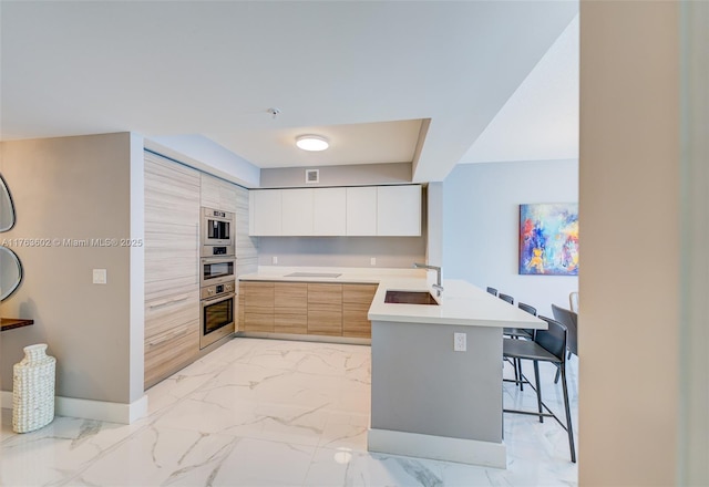 kitchen with marble finish floor, modern cabinets, a breakfast bar, a sink, and a peninsula