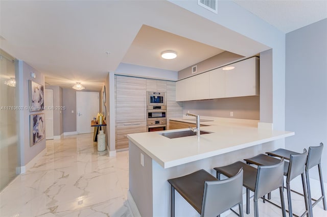 kitchen with visible vents, a breakfast bar, marble finish floor, modern cabinets, and a sink