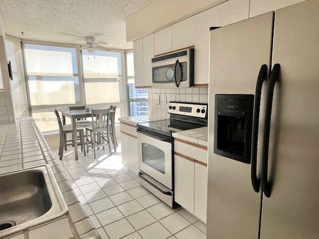 kitchen featuring backsplash, tile countertops, appliances with stainless steel finishes, light tile patterned floors, and ceiling fan