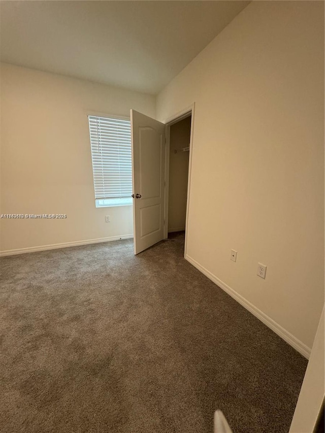 unfurnished room with dark colored carpet and baseboards