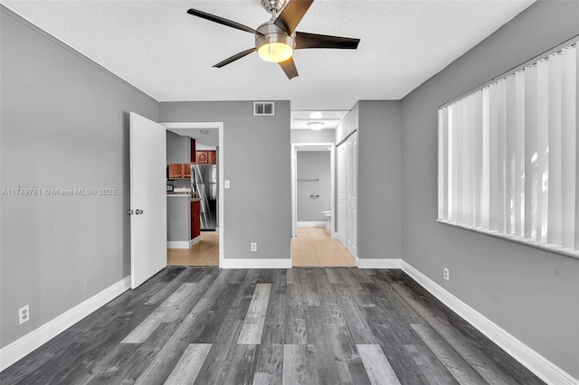 unfurnished bedroom featuring wood finished floors, baseboards, visible vents, freestanding refrigerator, and a textured ceiling