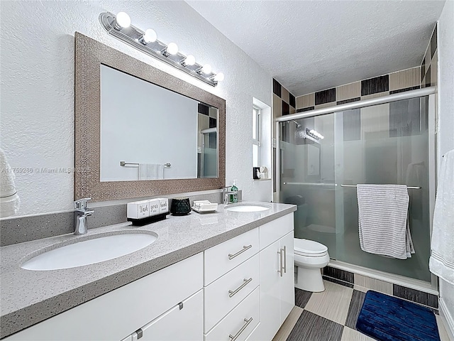 full bath with a textured ceiling, double vanity, a stall shower, and a sink