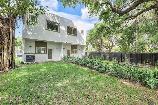 rear view of property with stucco siding, a lawn, and fence