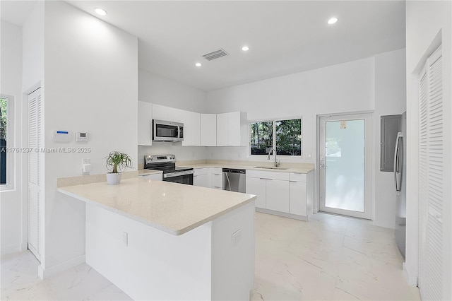 kitchen featuring marble finish floor, appliances with stainless steel finishes, a peninsula, white cabinets, and light countertops