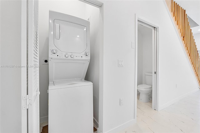 clothes washing area with baseboards, stacked washer and dryer, marble finish floor, and laundry area