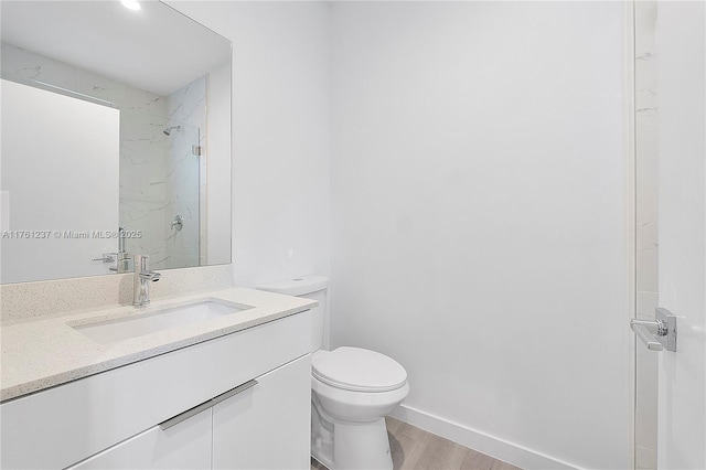 full bathroom with toilet, wood finished floors, a marble finish shower, baseboards, and vanity