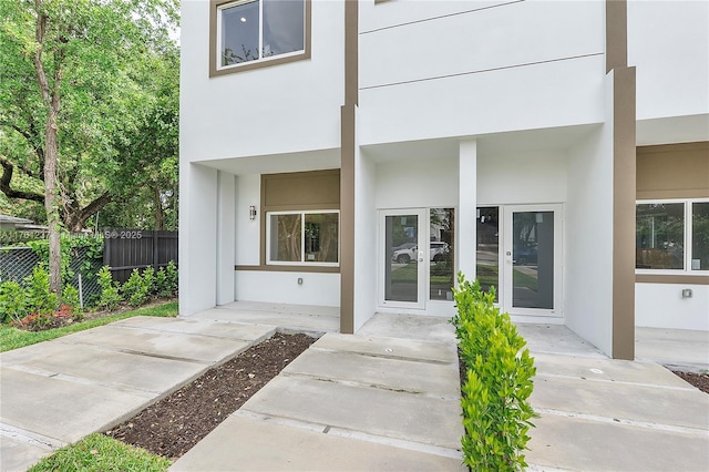 view of exterior entry featuring stucco siding, french doors, and fence