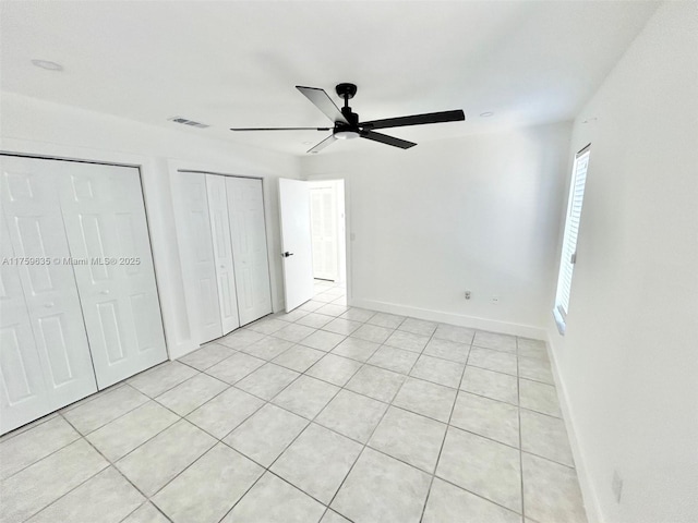 unfurnished bedroom featuring visible vents, multiple closets, light tile patterned floors, baseboards, and ceiling fan