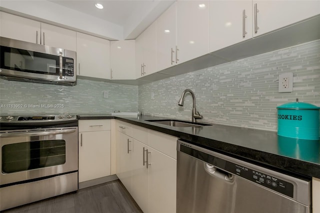 kitchen with a sink, dark countertops, backsplash, stainless steel appliances, and white cabinets