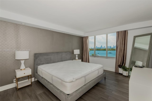 bedroom featuring wallpapered walls, dark wood finished floors, a water view, and an accent wall