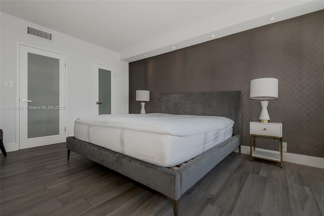 bedroom featuring an accent wall, wood finished floors, visible vents, and baseboards