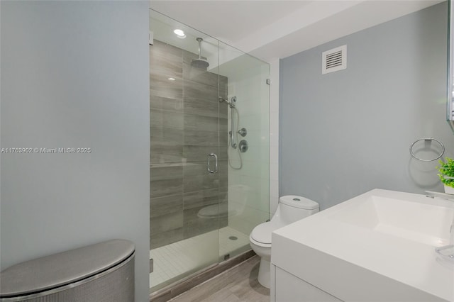 bathroom with vanity, a shower stall, toilet, and visible vents