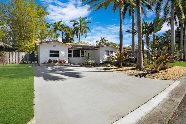 view of front of house featuring fence, concrete driveway, a front yard, stucco siding, and a chimney