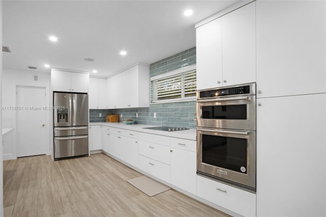 kitchen with light wood-type flooring, tasteful backsplash, stainless steel appliances, white cabinets, and light countertops