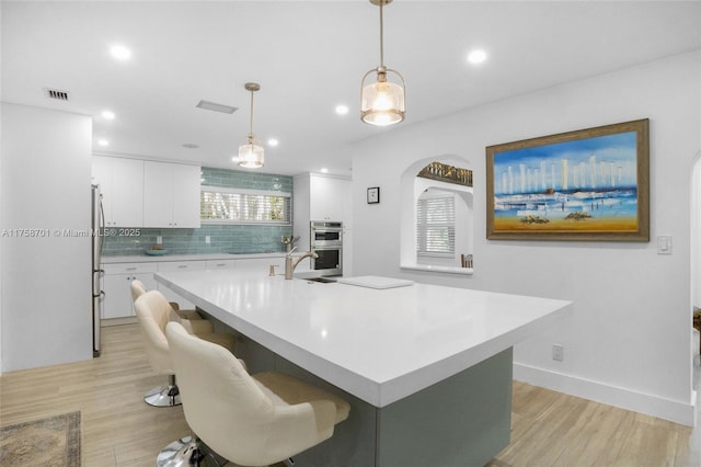 kitchen featuring light wood finished floors, light countertops, appliances with stainless steel finishes, white cabinetry, and tasteful backsplash