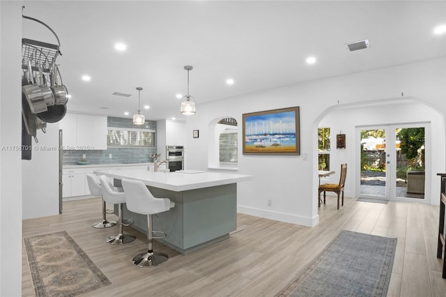 kitchen with visible vents, tasteful backsplash, white cabinetry, arched walkways, and light countertops