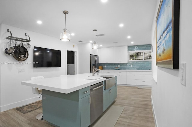 kitchen featuring tasteful backsplash, a center island with sink, light countertops, appliances with stainless steel finishes, and white cabinetry