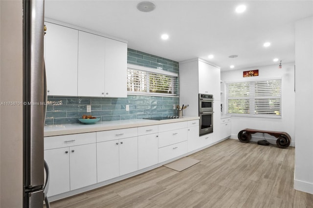 kitchen with light wood-type flooring, backsplash, white cabinetry, stainless steel appliances, and light countertops