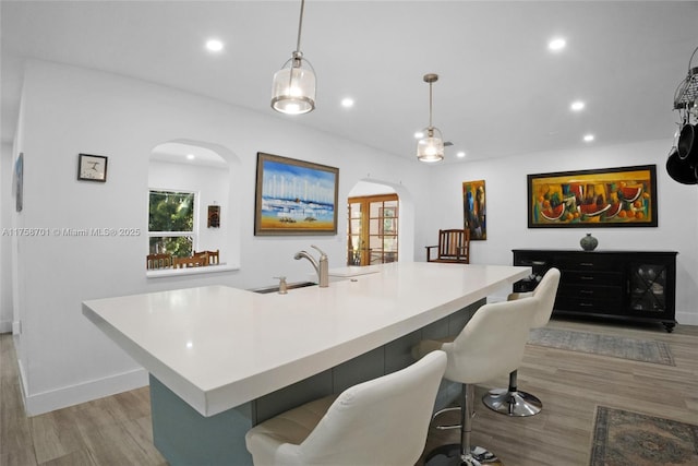 bar with baseboards, light wood-style flooring, recessed lighting, arched walkways, and decorative light fixtures