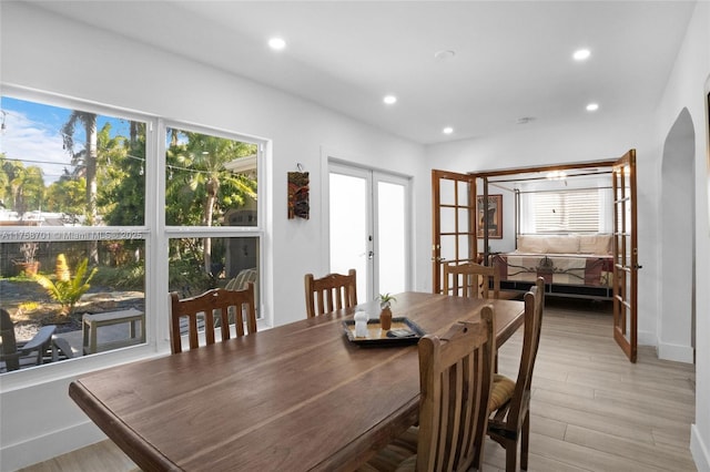 dining space with recessed lighting, french doors, arched walkways, and light wood-style floors