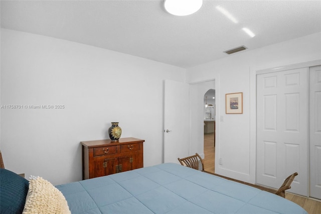 bedroom with wood finished floors, visible vents, arched walkways, and a closet