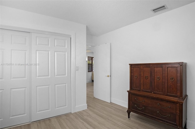 bedroom with light wood-type flooring, visible vents, a closet, arched walkways, and baseboards