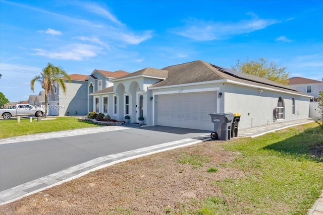 view of front facade featuring solar panels, stucco siding, concrete driveway, a front lawn, and a garage