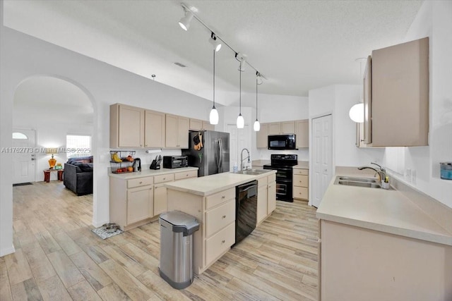 kitchen with a sink, black appliances, a center island with sink, and light wood finished floors