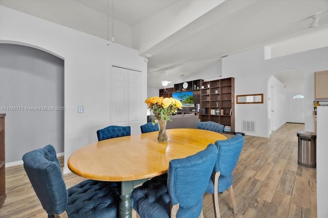 dining room featuring visible vents, baseboards, arched walkways, track lighting, and light wood-style floors