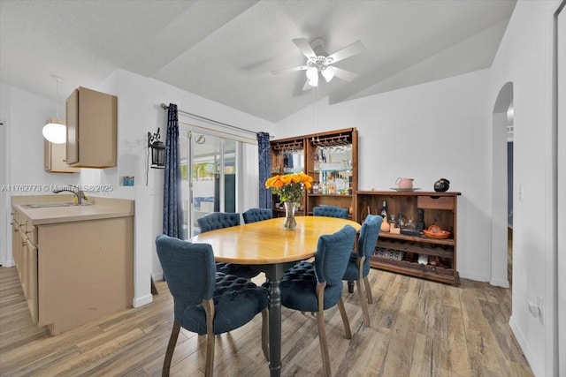 dining space with baseboards, light wood finished floors, arched walkways, ceiling fan, and vaulted ceiling