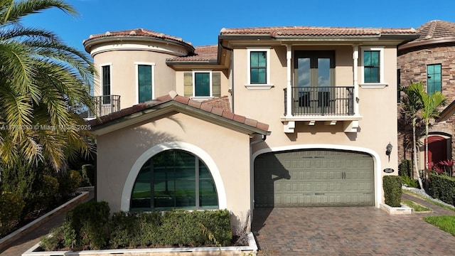 mediterranean / spanish-style home with a balcony, an attached garage, stucco siding, a tile roof, and decorative driveway