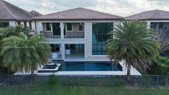 back of property with a balcony, stucco siding, a tiled roof, and a fenced backyard