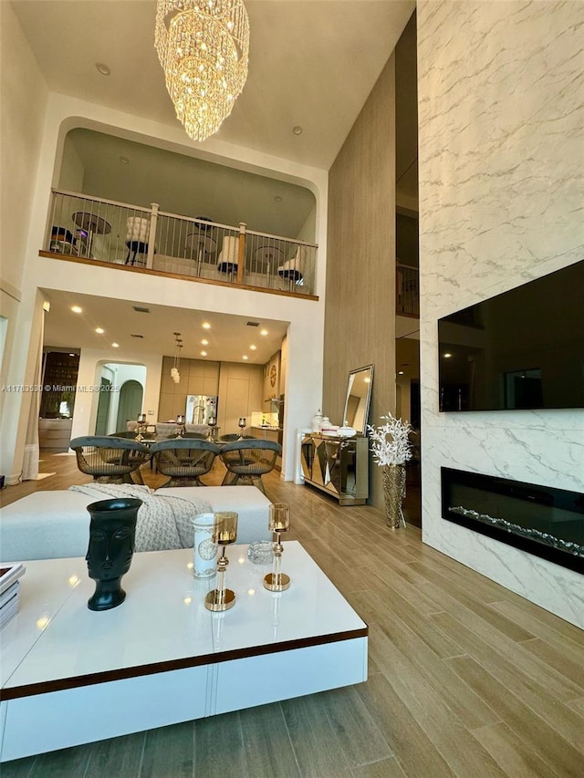 living area featuring a fireplace, wood finished floors, a towering ceiling, and a chandelier