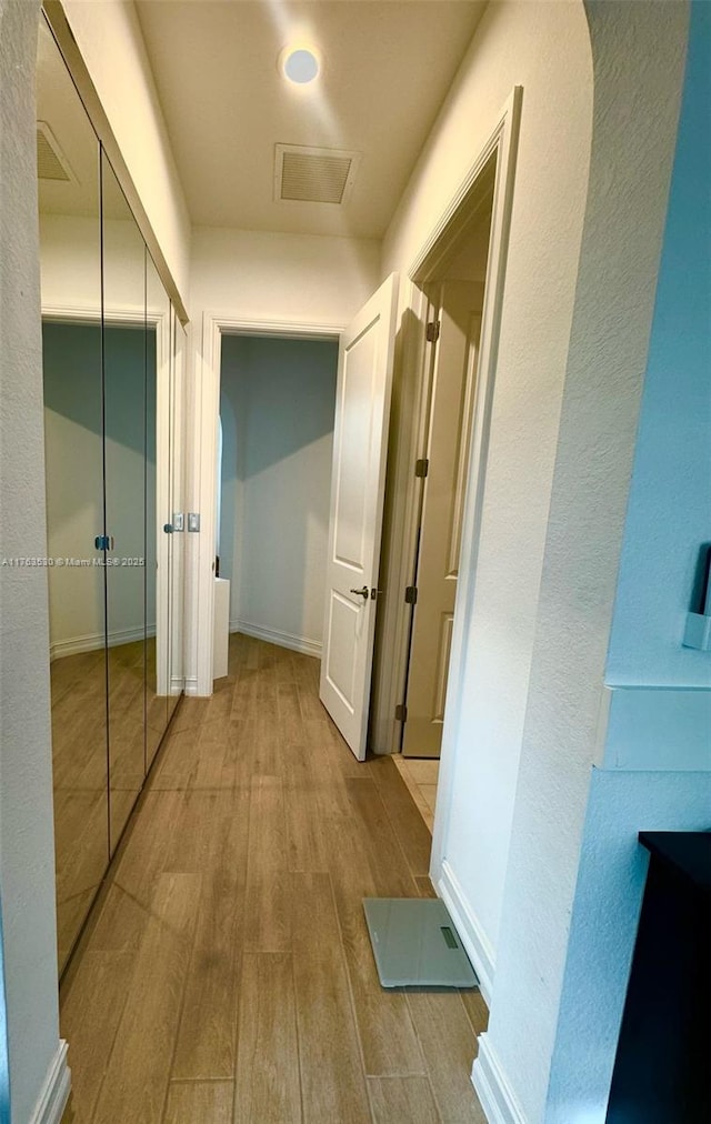 hallway featuring visible vents, baseboards, and wood finished floors