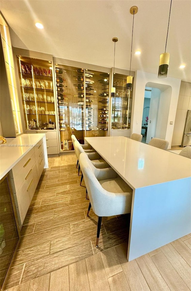 kitchen featuring wood finish floors, modern cabinets, decorative light fixtures, arched walkways, and light countertops